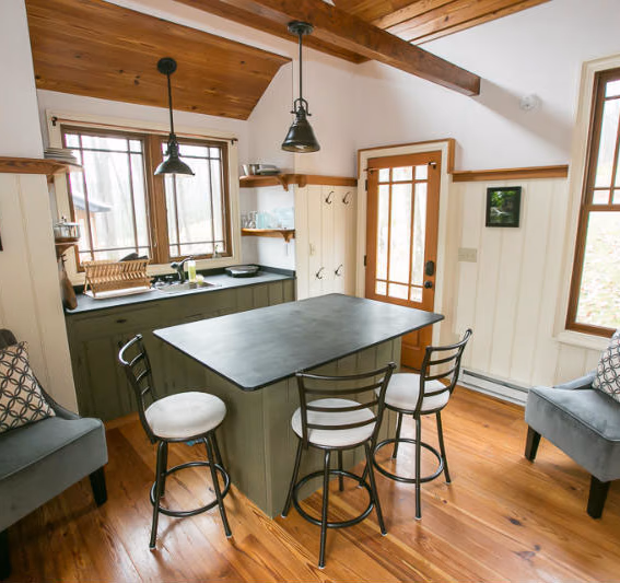 Inside a Blue Moon Rising cabin: a kitchen island with stools, armchairs, pine floors and exposed beams