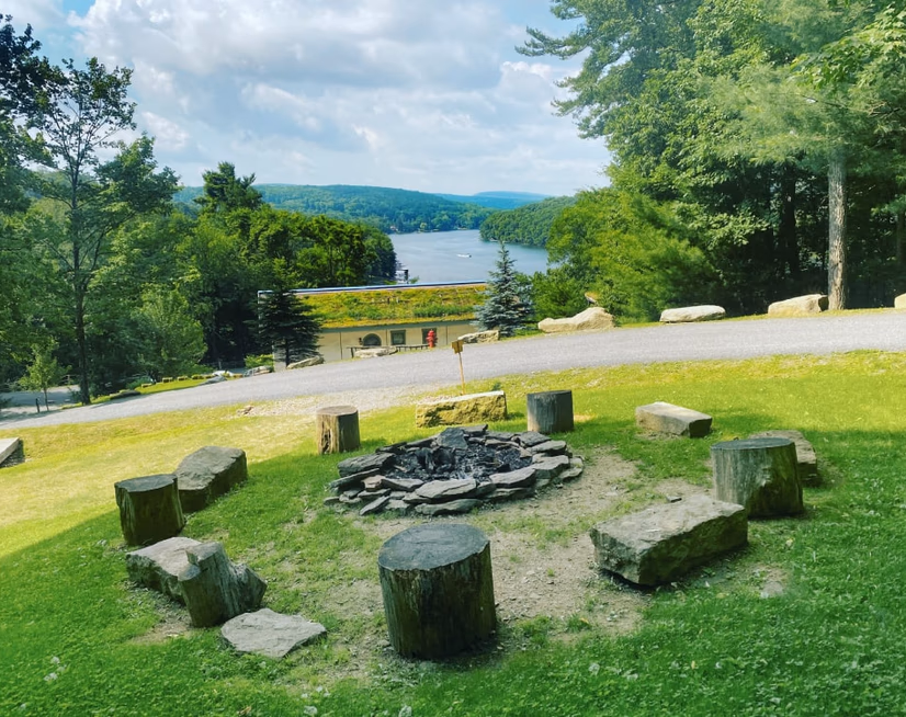 The communal fire pit ringed by log seats on a grassy slope, looking out over Deep Creek Lake